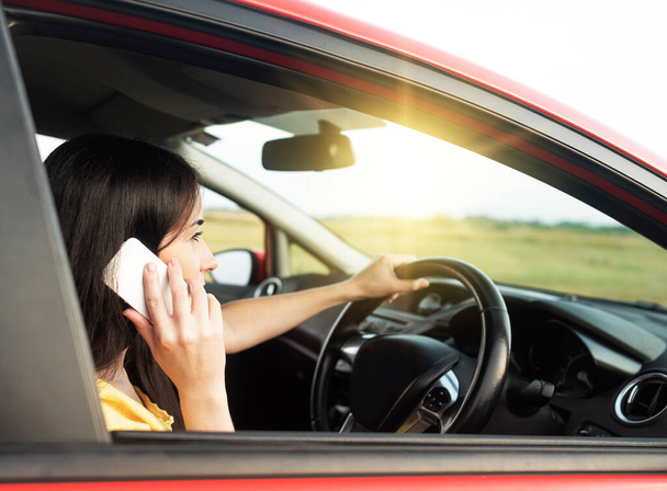 Mujer joven está utilizando un teléfono inteligente mientras conduce un coche. - Foto, Imagen
