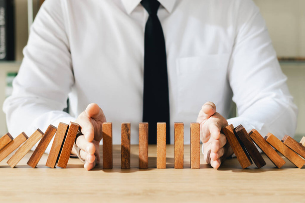 Risk management, business man hand Stop the continuous falling of wooden dominoes, stop the impact of the business crisis. hedging Solving business problems for success. - Foto, Imagem