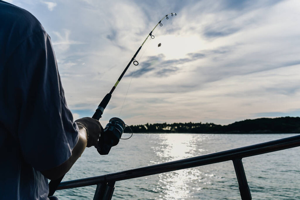 Horgászbot kerék közelkép, egy gyönyörű napfelkeltét halászó ember - Fotó, kép