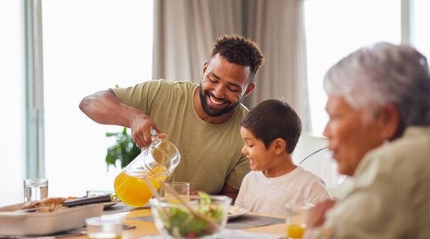 Closeup of a mixed race male and his son enjoying some food at the a table during lunch at home in the lounge. Hispanic father smiling and eating alongside his son at home. - Photo, Image