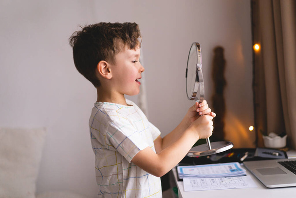 Speech therapy concept. Cute little boy pronouncing sound O looking at mirror doing an online Speech therapy lesson through a laptop - Fotó, kép