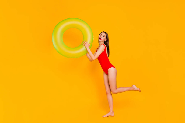 Full length photo of positive funky woman wear swimsuit rising green buoy isolated yellow color background. - 写真・画像