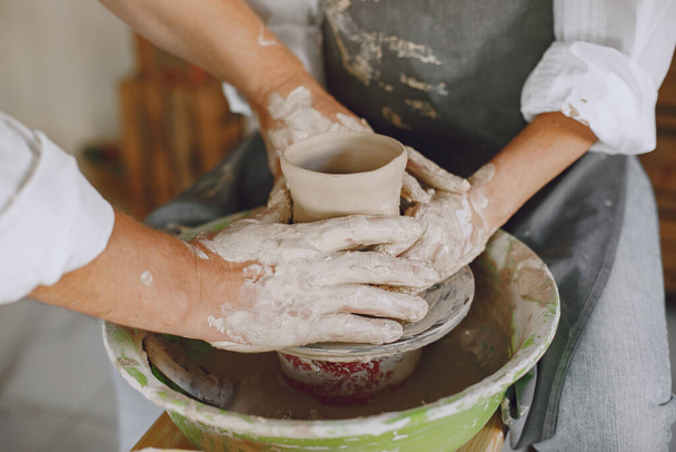 Mutual creative work. Adult elegant couple in casual clothes and aprons. People creating a bowl on a pottery wheel in a clay studio. - Foto, Imagen