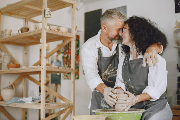 Mutual creative work. Adult elegant couple in casual clothes and aprons. People creating a bowl on a pottery wheel in a clay studio. - Fotó, kép