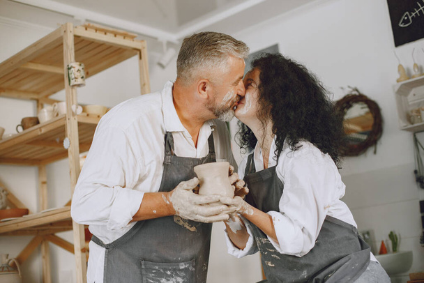 Mutual creative work. Adult elegant couple in casual clothes and aprons. People creating a bowl on a pottery wheel in a clay studio. - Φωτογραφία, εικόνα