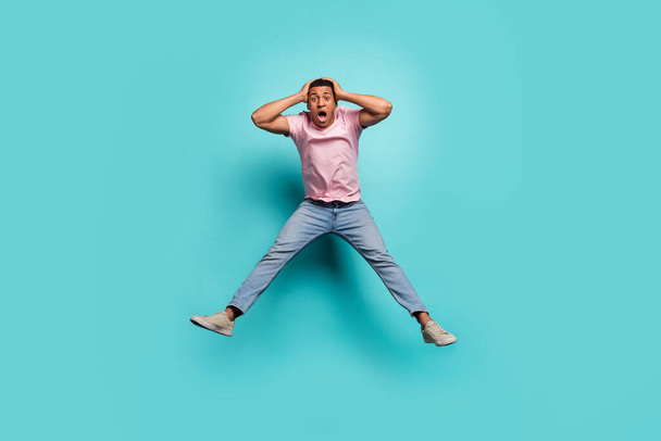 Full length photo of pretty impressed man dressed pink t-shirt jumping high arms hands head isolated turquoise color background. - Zdjęcie, obraz