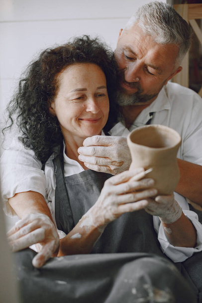 Mutual creative work. Adult elegant couple in casual clothes and aprons. People creating a bowl on a pottery wheel in a clay studio. - Foto, Imagem