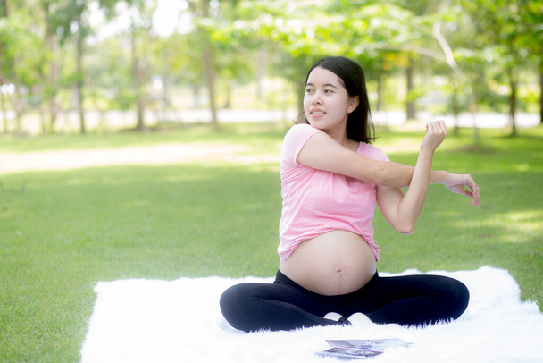Happiness young asian woman pregnant sitting doing sport exercise with stretch hands muscle for health care at park, mother practicing yoga for leisure in the garden, activity for pregnancy concept. - Photo, image