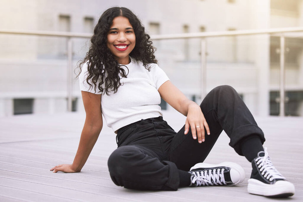 Beautiful mixed race fashion woman sitting outside in the city during the day. Young hispanic woman looking stylish and trendy, smiling and happy while outdoors in summer. Carefree and fashionable. - Fotografie, Obrázek