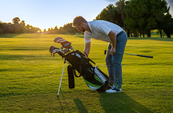 Молодой красивый мужчина на поле держит что-то в сумке для гольфа. - Фото, изображение