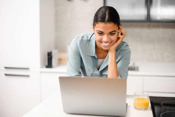 Smiling and concentrated businesswoman in casual wear is looking at the laptop screen, solving tasks, freelance woman working remotely from home - Photo, Image