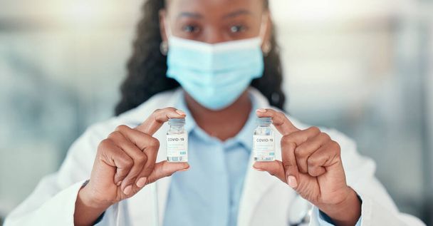 Medical doctor holding bottles of the covid cure. Ready to save the world from covid. African American doctor holding vials of the corona virus antidote.Healthcare professional wearing a mask. - Zdjęcie, obraz