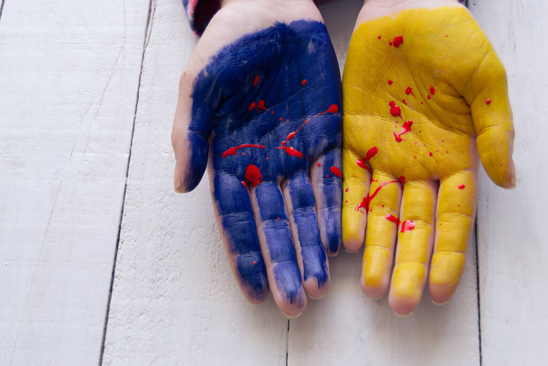 Close-up side view image of two female hands painted in Ukrainian blue and yellow colors with blood - Foto, Imagem
