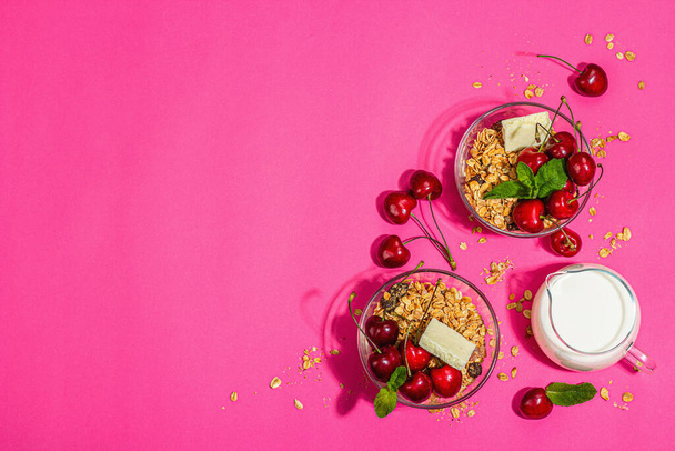 Summer breakfast concept. Healthy morning food. Ripe cherries, milk, white chocolate, and granola. A trendy hard light, dark shadow, pink background, top view - 写真・画像