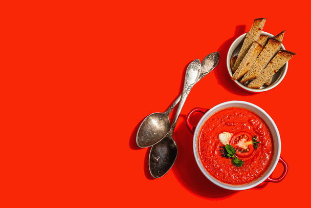 Sopa de tomate picante. Plato caliente vegano saludable, croutons, cubiertos vintage. Fondo rojo brillante, luz dura de moda, sombra oscura, vista superior - Foto, Imagen