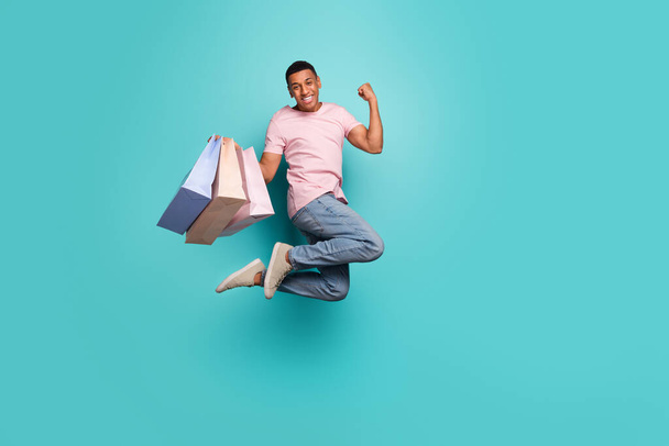 Full length photo of excited lucky man dressed pink t-shirt jumping rising fist shopping empty space isolated turquoise color background. - Fotó, kép