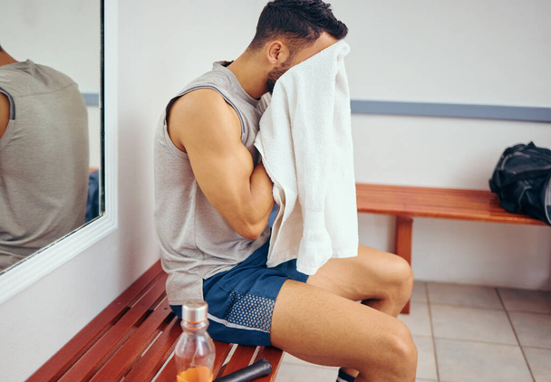 Young player wiping his face with a towel. Tired man cleaning his face with a towel after a squash match. Squatch player sitting in his gym locker room. Mixed race man taking a break after a match. - Φωτογραφία, εικόνα