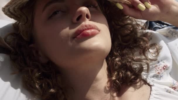 Portrait of sleepy cute girl covering curly head with straw hat from summer sunlight. Attractive relaxed lady lying beach wearing flowery dress close up. Calm young woman relax on sunny nature. - Filmmaterial, Video