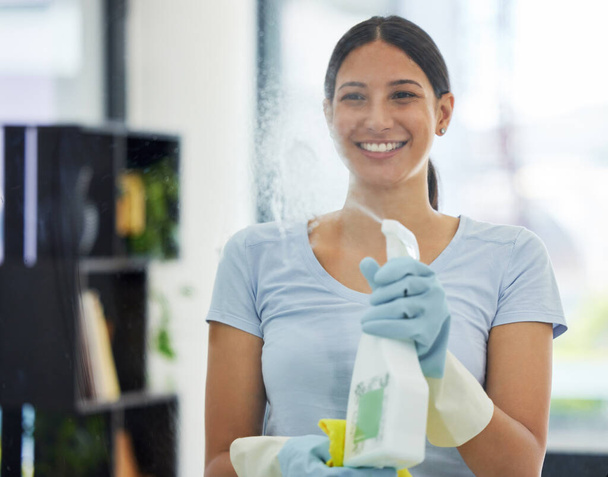 Portret van een gelukkige gemengde ras huishoudelijk werker met behulp van een doek op een raam. Een Spaanse vrouw die graag klusjes doet in haar appartement.. - Foto, afbeelding