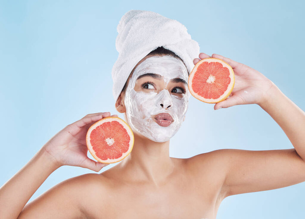 Beautiful young mixed race woman wearing a face mask peel and towel while posing with a grapefruit. Attractive female clean and fresh out the shower and applying her daily skincare regime to her face. - Fotografie, Obrázek