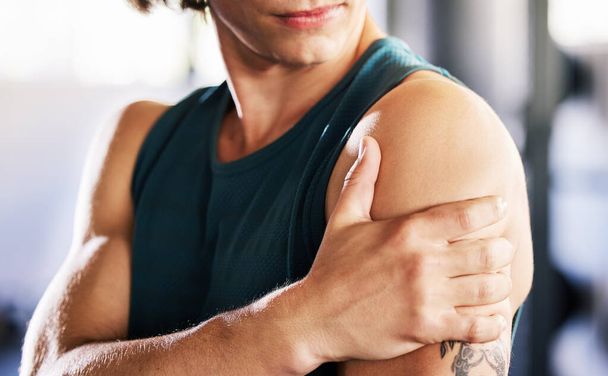 Closeup of one caucasian man holding his sore shoulder while training in a gym. Guy suffering with painful arm injury from fractured joint and inflamed muscles during workout. Struggling with stiff - Foto, imagen