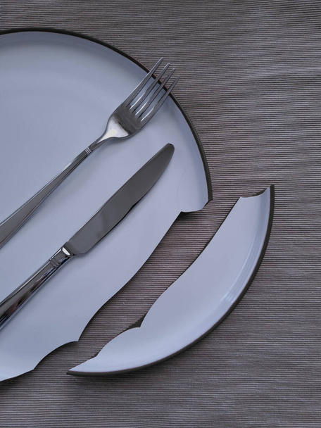 Tableware lay over the broken plate. Knife and fork on the dining plate. Misfortune in the kitchen. - 写真・画像