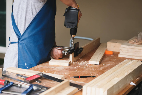 Les entrepreneurs du travail du bois utilisent une perceuse à travers les trous de bois pour assembler et construire des tables en bois pour les clients. - Photo, image