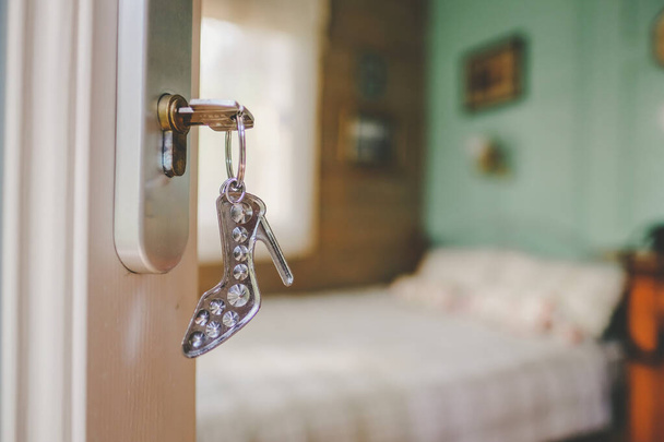 Hotel room and keys in the door with a keychain - a stylized womans high-heeled shoe. Prostitution, extramarital affairs. Defocused. High quality photo - Photo, Image