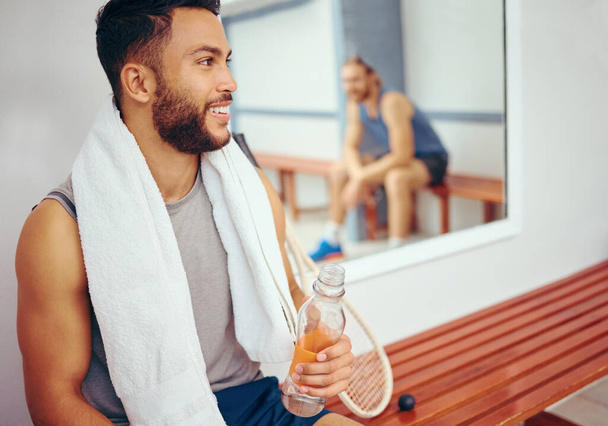 Happy friends relaxing after a match. Mixed race player drinking water after a match with his friend. Two friends talking after a squash match. Coach talking to his player in the locker room. - Photo, image