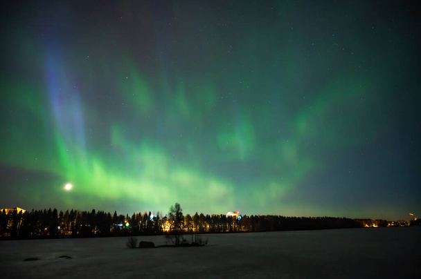 A various colour geomagnetic Aurora borealis on the starry night sky over a city. Aurora Borealis over Swedish lake Islands. Northern Sweden. Wintertime starry sky. - Zdjęcie, obraz