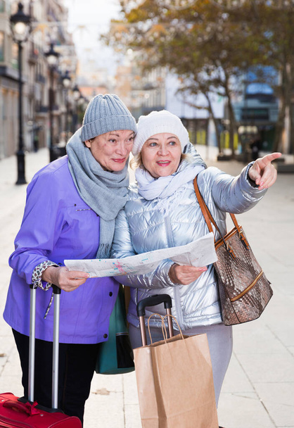 Senior woman with female friend traveling together looking for destination with city map. - Fotó, kép