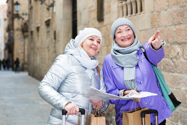 Two positive elderly women tourists with city guide walking on street - Foto, immagini