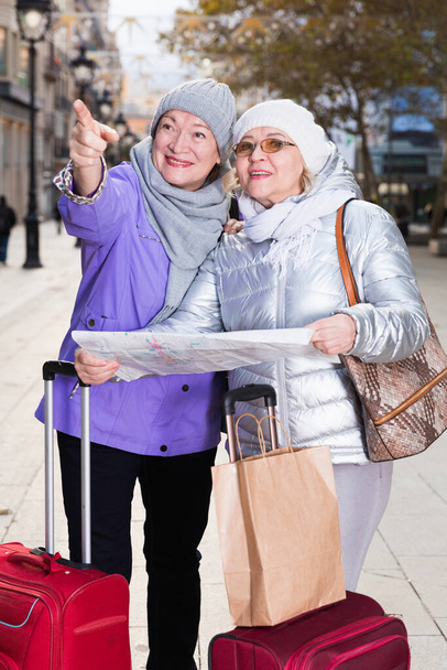 Senior vrouw met vrouwelijke vriend samen op zoek naar bestemming met stadsplattegrond. - Foto, afbeelding
