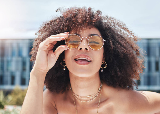 Jonge gemengde ras vrouw met krullend natuurlijk afro haar dragen trendy en stijlvolle zonnebril buiten. Eén vrouwtje ziet er alleen zorgeloos, koel en zelfverzekerd uit. Gelukkige modieuze Spaanse vrouw in de stad. - Foto, afbeelding