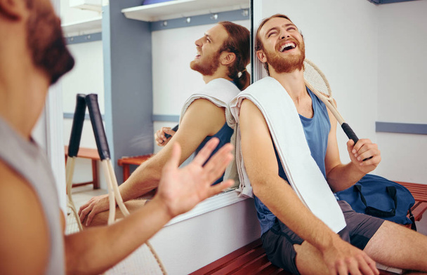 Cheerful squash players laughing and talking. Two friends taking a break from their match to relax. Happy friends bonding in the gym locker room. Two men bonding before playing a game of squash. - Fotoğraf, Görsel