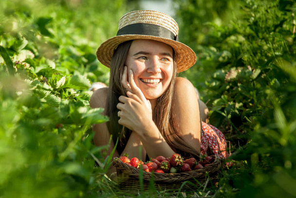 girl in strawberry field with basket of fresh picked berries - Foto, afbeelding