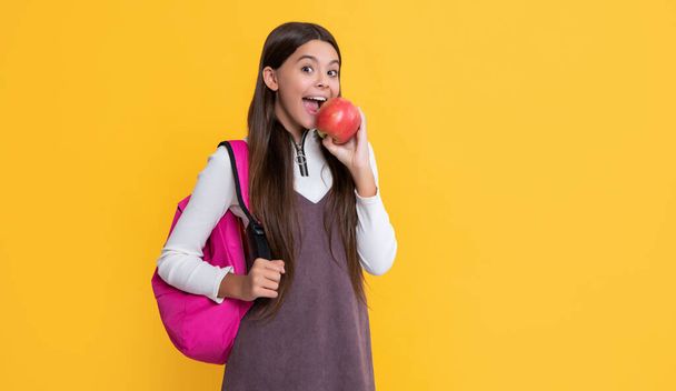 здивована дитина з шкільним рюкзаком і яблуком на жовтому фоні
. - Фото, зображення
