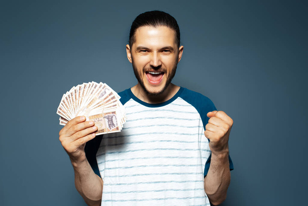 Portrait of happy man holding money, Moldovan banknotes, on blue. Yes gesture. - Foto, Imagen