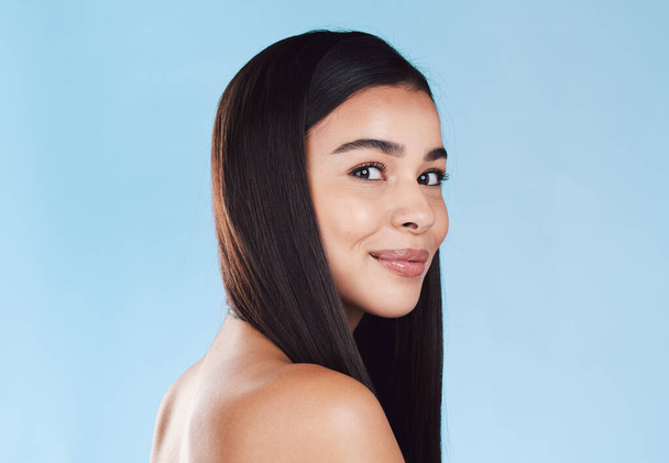 Portrait of one beautiful young hispanic woman with healthy skin and sleek hair smiling against a blue studio background. Happy mixed race model with flawless complexion and natural beauty. - Fotó, kép