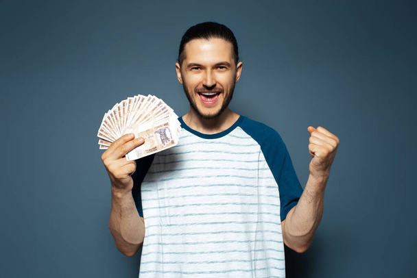 Portrait of happy man holding money, Moldovan banknotes, on blue. Yes gesture. - 写真・画像