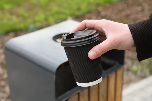 Man throwing black paper cup into trash can outdoors, closeup. Space for text - Zdjęcie, obraz