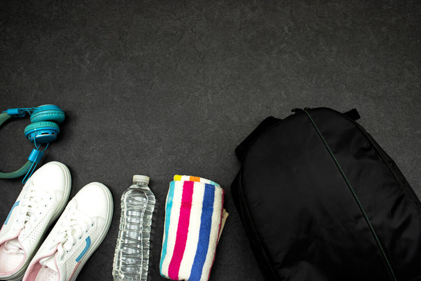 Sağlıklı yaşam tarzı, spor veya atlet ekipmanları seti: siyah sırt çantası ve mavi kablosuz kulaklık ve havluyla bir şişe su, gri arka planda spor ayakkabıları - Fotoğraf, Görsel