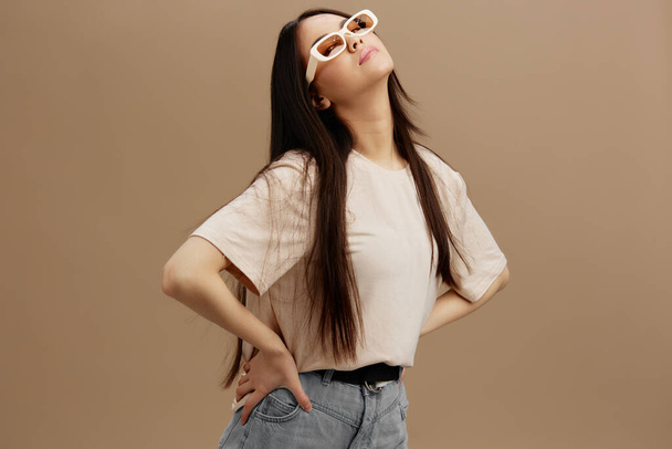 Nuori nainen beige T-paita lasit aiheuttaa vaatteita muoti beige tausta. Laadukas kuva - Valokuva, kuva