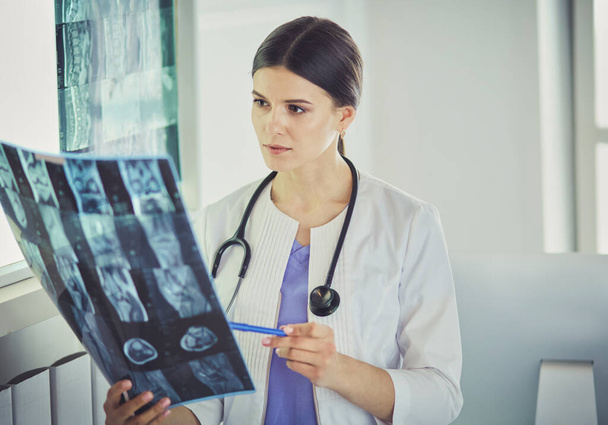 Jeune femme médecin souriante avec stéthoscope pointant vers la radiographie au cabinet des médecins
 - Photo, image