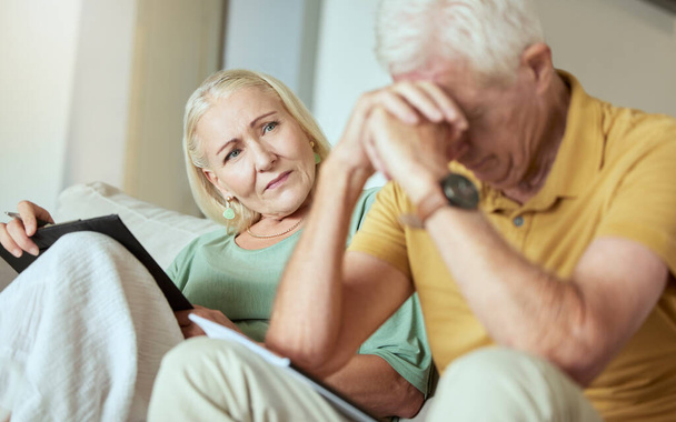 Ein unglückliches älteres Paar sitzt zusammen auf einem Sofa und sieht gestresst aus. Ältere kaukasische Männer und Frauen machen sich Sorgen um ihre Zukunft, während sie Papierkram und ihre Schulden betrachten. - Foto, Bild