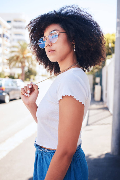Young stylish mixed race woman with curly natural afro hair wearing trendy glasses outside. One female only looking carefree, cool and confident. Happy fashionable hispanic woman standing in the city. - Fotografie, Obrázek