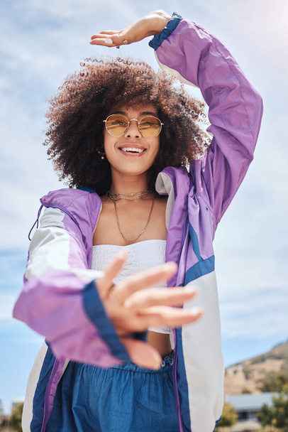 Portrait of young trendy beautiful mixed race woman with an curly afro smiling and posing alone outside. Hispanic woman wearing sunglasses and feeling happy. One fashionable African American woman - Foto, Bild