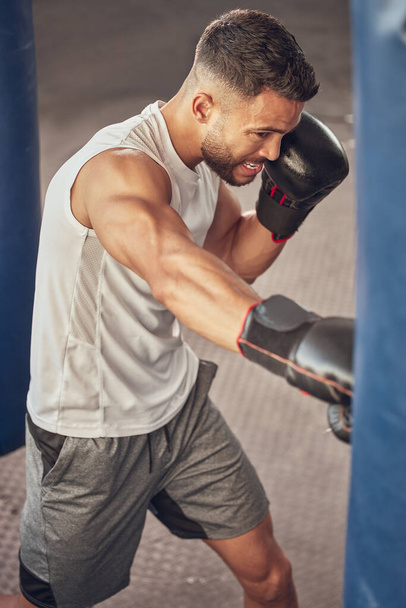 Boxer hitting a punch bag in the gym. Strong mma fighter punching in the gym. Combat fighter cardio training in the gym. Muscular athlete boxing practice in the gym. Fit man with power punch. - Fotó, kép