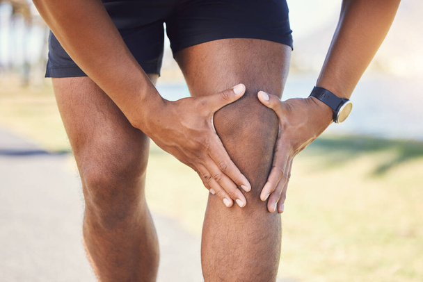 Closeup of unknown fit active mixed race man holding his knee in pain. Unrecognizable athlete suffering from discomfort from a bad knee injury. Arthritis causing him to hold his leg while exercising. - Photo, image