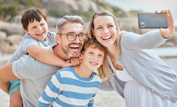 Felices padres caucásicos y niños tomando selfies mientras se relajan en unas divertidas vacaciones de verano en familia juntos en la playa. Padres amorosos que capturan fotos e imágenes para recuerdos especiales de la infancia mientras - Foto, Imagen